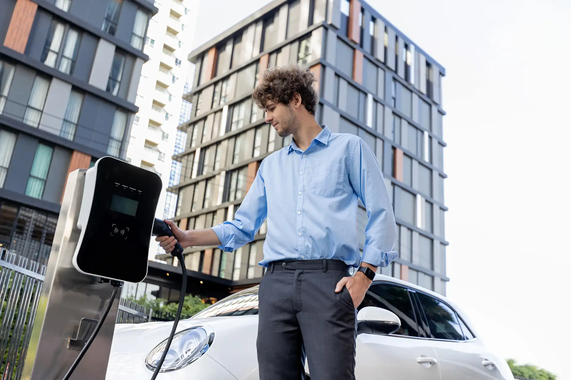 Homme chargeant sa voiture électrique à une borne de recharge dans un environnement urbain